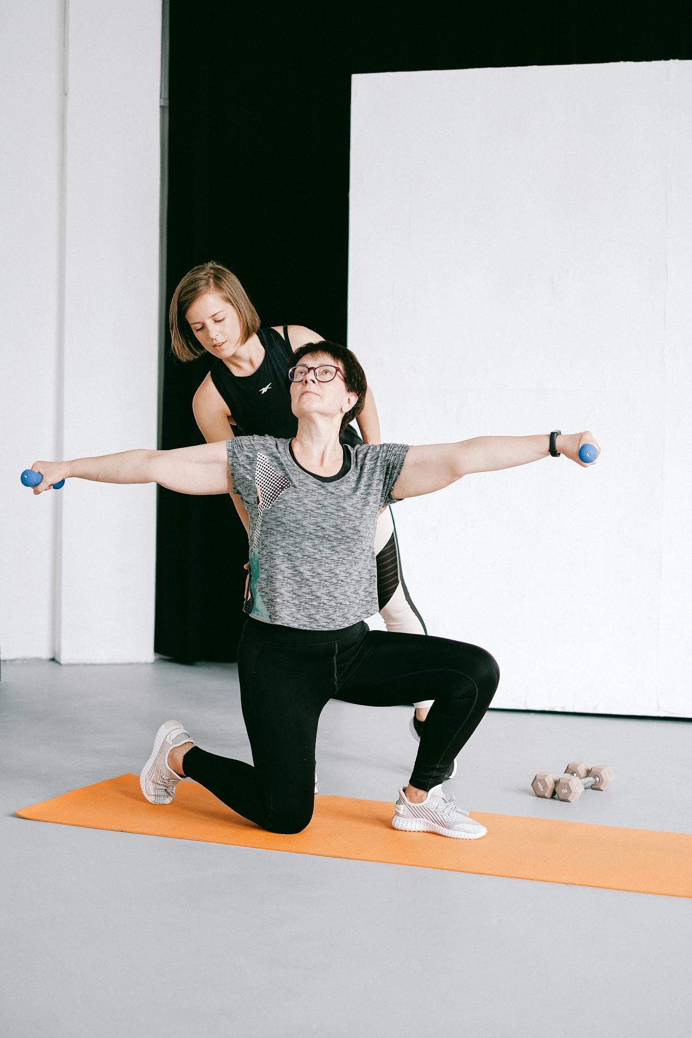 A personal trainer guides a woman during an arm workout with dumbbells in a studio.