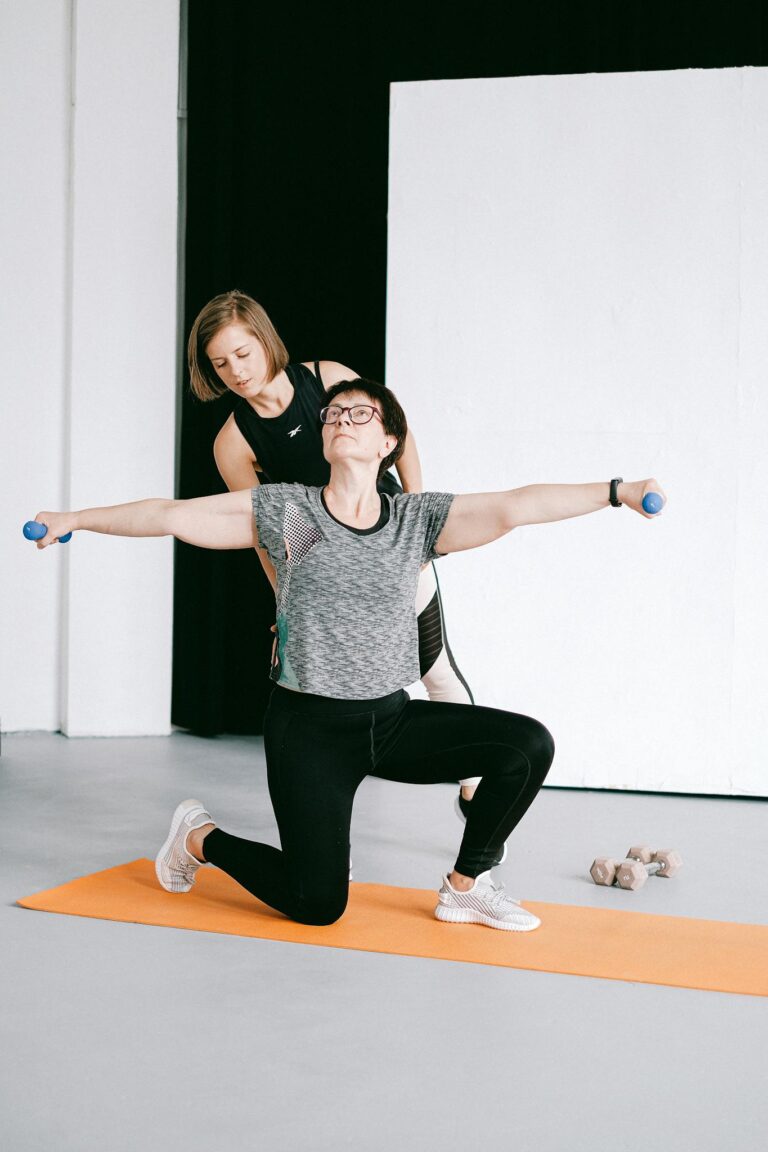 A personal trainer guides a woman during an arm workout with dumbbells in a studio.